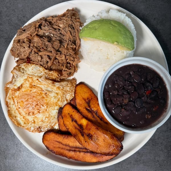 Venezuelan Pabellón Criollo with shredded beef, rice, avocado, fried eggs, plantains, and black beans.