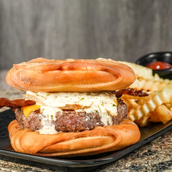 Calle El Hambre's Venezuelan burger with bacon, cheese, and sauce, served with waffle fries.