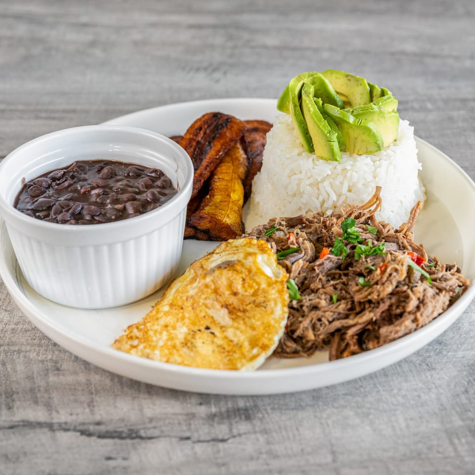 Venezuelan Pabellón Criollo with shredded beef, rice, black beans, fried egg, plantains, and avocado.